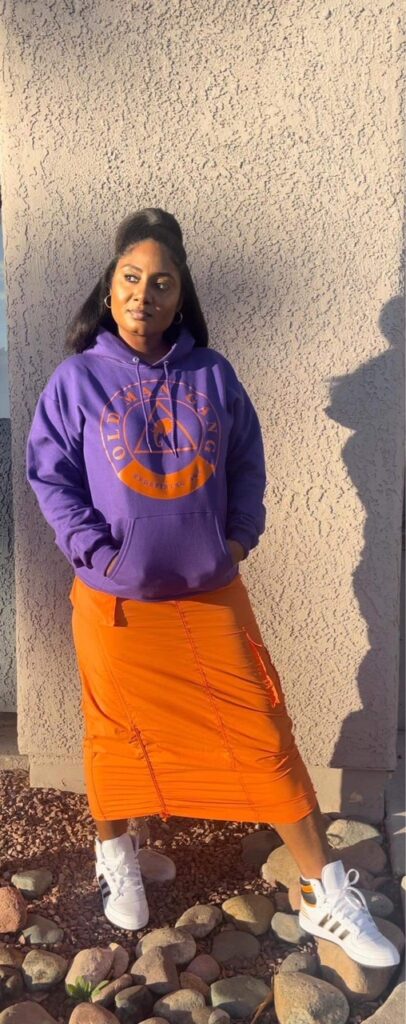 A woman in an orange skirt and purple hoodie.