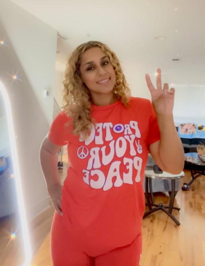 A woman in an orange shirt is giving the peace sign.