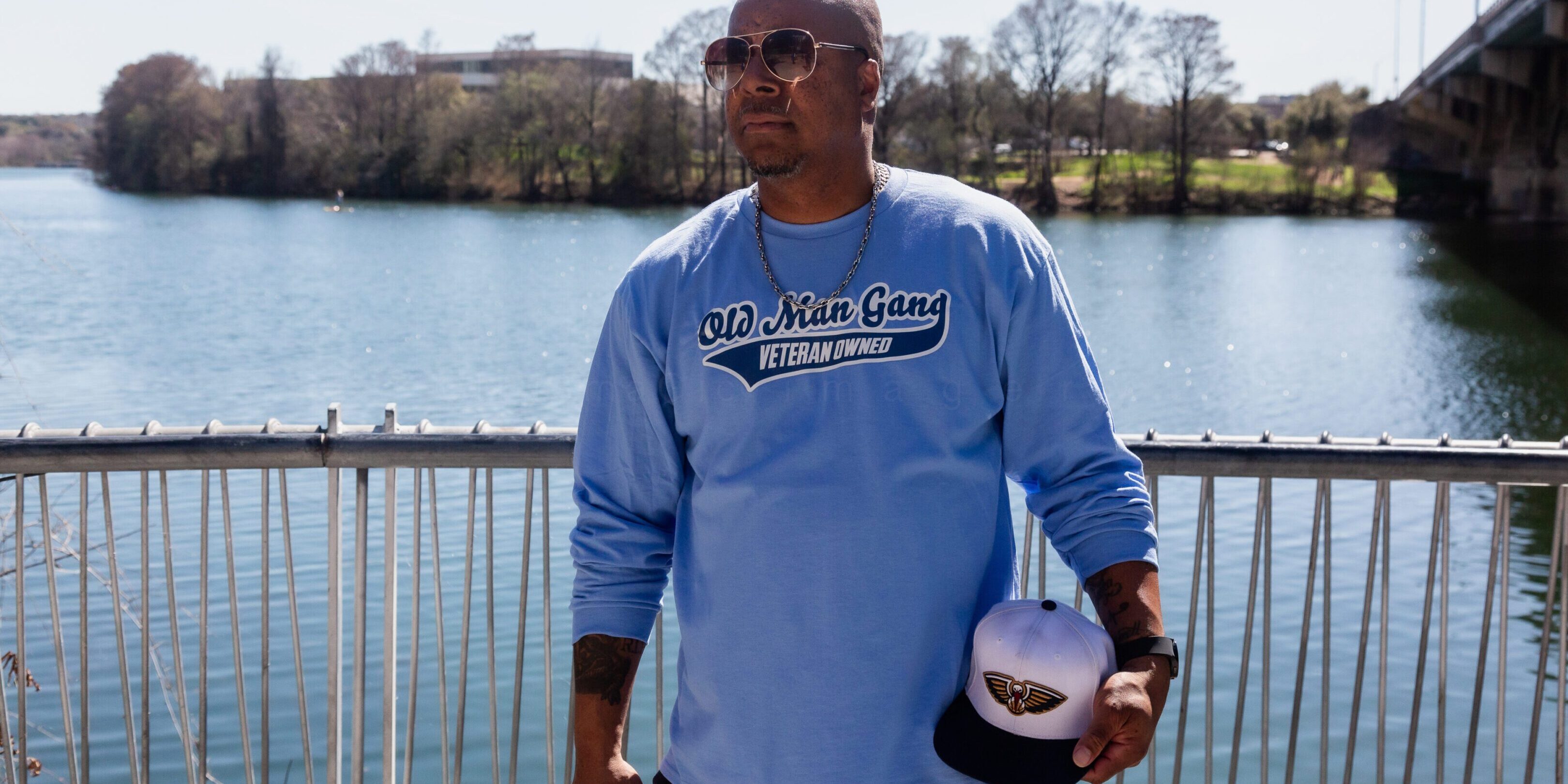 Man in sunglasses holding a basketball by a riverside fence.